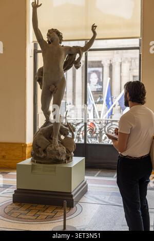 Parigi, Francia - 2 maggio 2026: Una persona si trova di fronte a una scultura all'interno di un museo. La figura è alta e raffigura una forma maschile. Arriva la luce naturale Foto Stock