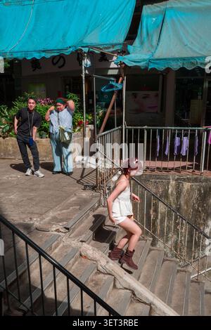 Una donna con i capelli tinti scende le scale di cemento in un vicolo urbano mentre due persone guardano. Foto Stock