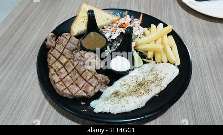 Pasto completo con bistecca di manzo alla griglia con patatine fritte su piatto in ceramica nera Foto Stock
