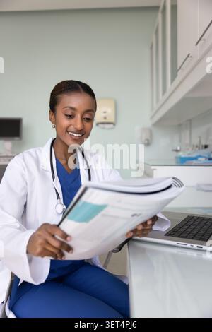 Positivo giovane donna afroamericana medico che esamina un grande libro di testo Foto Stock