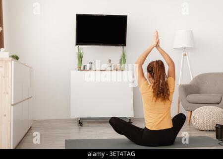 Inriconoscibile giovane donna che si allunga sul tappetino da yoga a casa per la routine fitness Foto Stock