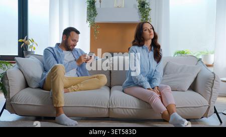 Infastidita insoddisfatta donna caucasica offesa seduta vicino a un uomo occupato con gadget per telefoni cellulari che ridono guardando divertente video ridere smartphone Foto Stock