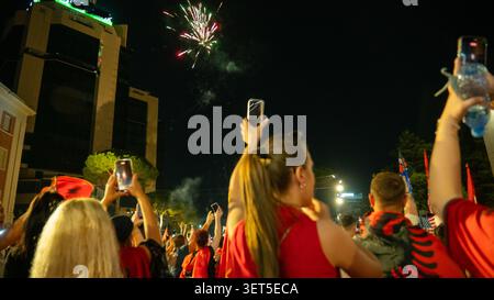 Tirana, Albania – 20 giugno 2026: I manifestanti trattengono i telefoni cellulari mentre i fuochi d'artificio appaiono sopra una protesta notturna nel centro della città. Foto Stock