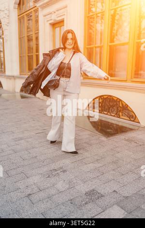 Donna che cammina in città elegante giovane donna passeggiando con sicurezza su un marciapiede di pietra durante l'ora d'oro in un ambiente classico della città Foto Stock