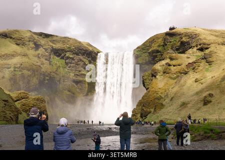 Turisti che fotografano la famosa cascata di Skogafoss nel sud dell'Islanda. Foto Stock
