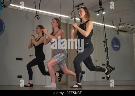 Due donne si allenano insieme con le cinghie di sospensione, mantenendo l'equilibrio in un esercizio di affondo controllato. L'immagine mette in evidenza l'assistenza clienti e i progressi personali Foto Stock