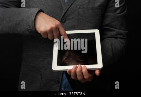Persona che punta verso il tablet mentre indossa un abbigliamento formale su sfondo scuro Foto Stock