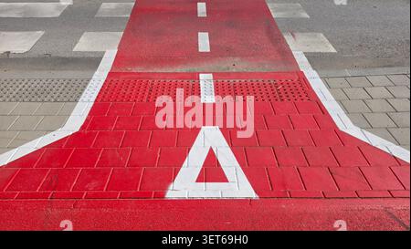 Una vista dall'alto dettagliata mostra una pista ciclabile rossa con lastre di pavimentazione tattili e un cartello di segnalazione bianco dipinto a triangolo in una città Foto Stock