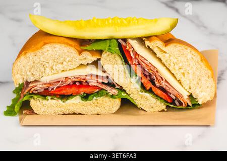 Abbondante panino con affettati, provolone, lattuga, pomodoro, cipolla, e pepe rosso su un panino morbido servito con una lancia di sottaceti. Foto Stock
