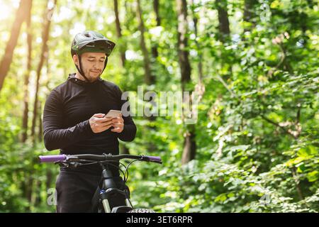 Giovane pilota in piedi in foresta, con il telefono cellulare Foto Stock