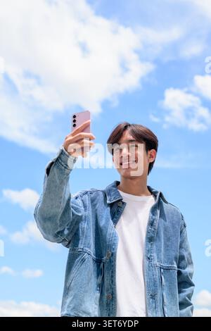 Fotografia di stile di vita verticale a basso angolo di un bel giovane tailandese del sud-est asiatico Isan non binario che sorride felicemente e guarda la fotocamera mentre h Foto Stock