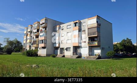 Un'immagine grandangolare e bassa di un edificio residenziale in cemento per famiglie con balconi chiusi e dettagli arancioni circondati da un grande verde Foto Stock