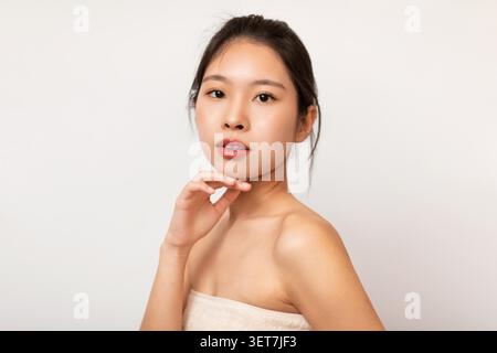 Giovane donna asiatica che posa splendidamente con la mano vicino al Chin, sfondo pulito, concetto di bellezza Foto Stock