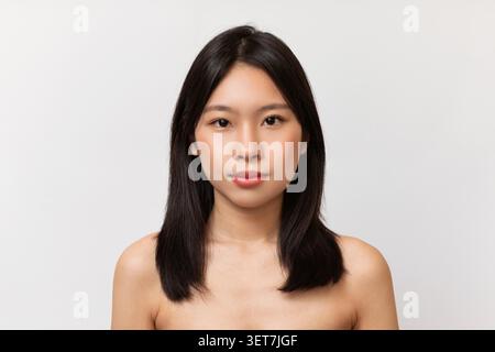 Giovane donna asiatica con capelli lunghi che guarda fiduciosa, sfondo studio, concetto di bellezza Foto Stock
