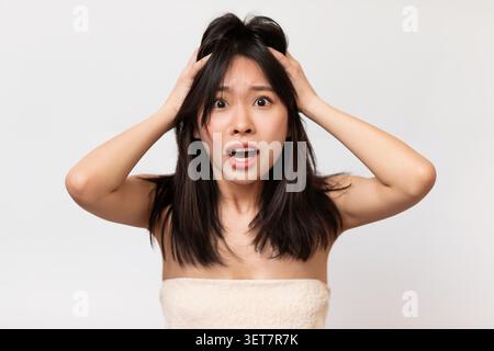 Stressata giovane donna asiatica con le mani sulla testa che sembra scioccata e sopraffatta Foto Stock