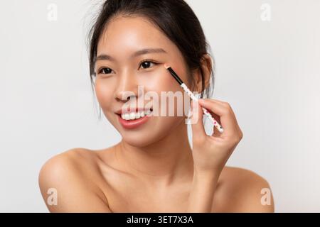 Sorridente giovane donna asiatica applicazione trucco con Brush, concetto di bellezza Foto Stock