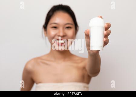 Donna asiatica sorridente che tiene il bastone deodorante bianco in bagno, concetto Skincare Foto Stock