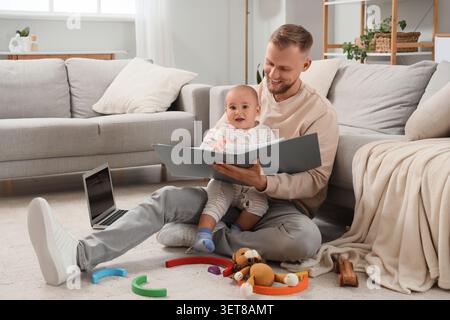 Padre felice e figlio piccolo leggono insieme un libro sul pavimento, legami familiari e sviluppo della prima infanzia, il padre sorride mentre tiene il libro Foto Stock