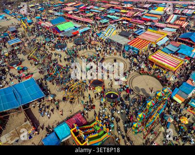 Vista aerea di una vivace zona fieristica con bancarelle colorate, varie giostre e folle di persone che camminano attraverso i terreni sabbiosi di Bog Foto Stock