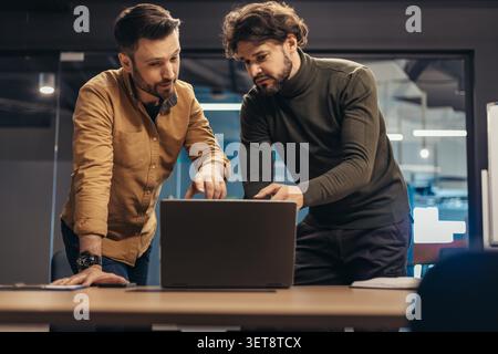 Due uomini concentrati che collaborano al concetto di notebook in ufficio moderno, business Foto Stock
