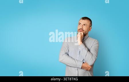 Uomo caucasico di mezza età che contempla sfondo blu, espressione premurosa, concetto di business Foto Stock