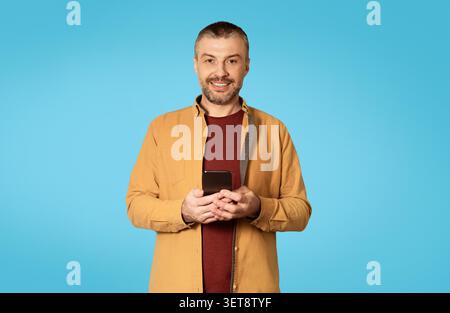 Uomo sorridente di mezza età con smartphone in mano, espressione felice, concetto aziendale Foto Stock