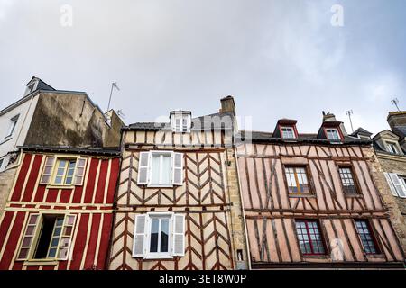 Ripresa ad angolo basso di tre storiche case incorniciate in legno a Vannes, Bretagna. Le facciate medievali mostrano travi geometriche in legno, rosso e rosa vivaci Foto Stock