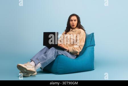Sorpresa giovane donna che lavora su un notebook mentre è seduta su una borsa di fagioli, Focused Expression Foto Stock