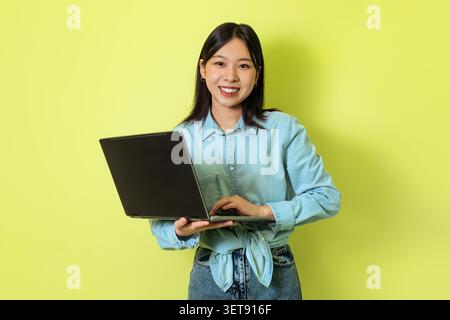 Giovane donna asiatica che utilizza notebook e sorride, concetto aziendale, sfondo verde Foto Stock