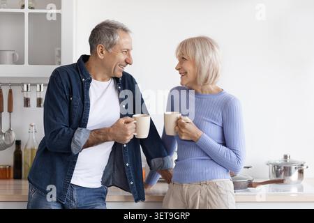 Felice coppia senior sorridente e tiene insieme le tazze da caffè in cucina, concetto di famiglia Foto Stock