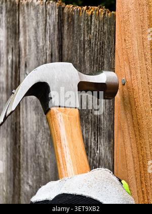 Martello che inserisce il chiodo nel pannello di recinzione in legno durante il progetto di costruzione all'aperto Foto Stock