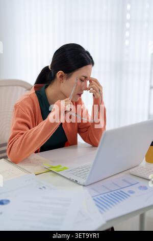 Stanca donna d'affari asiatica che soffre di stress lavorativo esaurimento durante l'analisi dei documenti di dati nello spazio di lavoro Foto Stock