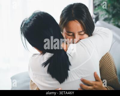 Primo piano di una donna asiatica che abbraccia una giovane donna a casa, mostra conforto, perdono, amore familiare, guarigione emotiva, empatia, supporto, fiducia, ricostruzione Foto Stock