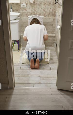La donna si inginocchia in bagno e soffre di malattia o malattia mattutina Foto Stock