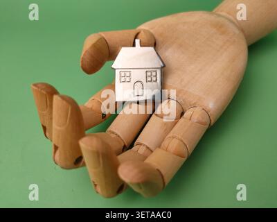 Un modello di casa in argento in miniatura si trova in sicurezza nel palmo aperto di una mano di manichino in legno articolato. Foto Stock