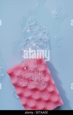 Spugna in schiuma rosa su sfondo blu con bolle di liquido e sapone Foto Stock