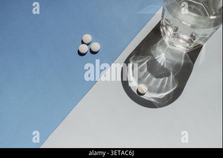 Un singolo tablet e un bicchiere di acqua fresca su uno sfondo minimalista blu bicolore Foto Stock