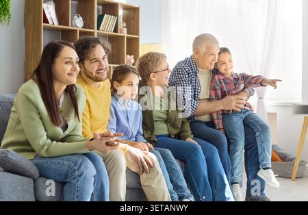 Famiglia felice e multigenerazionale che guarda la TV insieme sul divano in un luminoso soggiorno Foto Stock