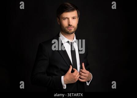 Uomo sicuro di sé in un abbigliamento formale che adatta la sua tuta a sfondo scuro Foto Stock