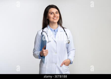 Dottoressa sorridente in cappotto bianco che regge gli appunti con un comportamento amichevole Foto Stock
