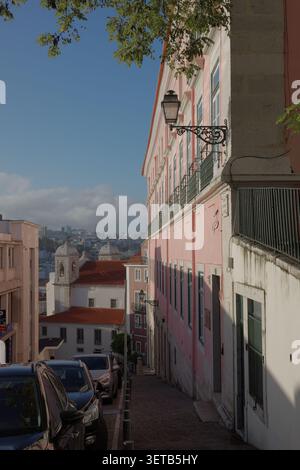 Facciata dell'edificio rosa con tende verdi, staffa decorata per lampada da parete in ferro e albero contro cielo blu a Lisbona Foto Stock
