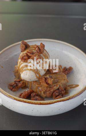 Dessert caramellato con gelato, noci candite e salsa di caramello su piatto di ceramica, Lisbona Foto Stock