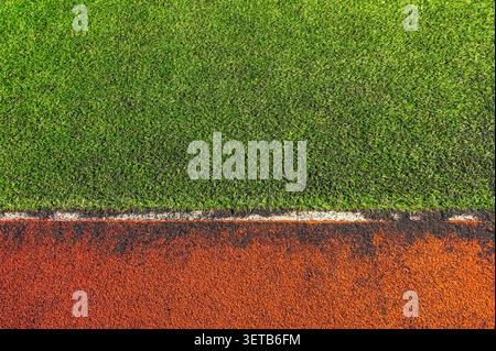Vista dall'alto del tappeto erboso verde artificiale e pista da corsa in gomma rossa usurata. Il vecchio confine del campo dello stadio è diviso dalla linea bianca. Foto Stock