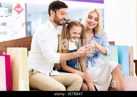 La famiglia ama fare shopping insieme mentre guarda uno smartphone in un moderno spazio retail Foto Stock