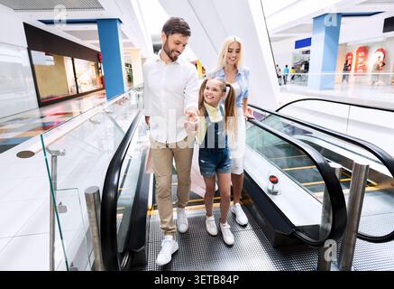 La famiglia si diverte insieme in un centro commerciale mentre utilizza l'escalator Foto Stock