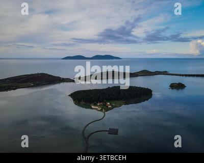 Un drone aereo cattura il Monastero di Santa Maria su una piccola isola densamente boscosa nella laguna di Butrint, collegata da un tortuoso wal di legno Foto Stock
