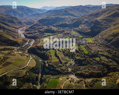 Un'ampia vista aerea cattura l'Osum Canyon e la sua valle circostante, mostrando un fiume tortuoso, campi agricoli e un piccolo villaggio nes Foto Stock
