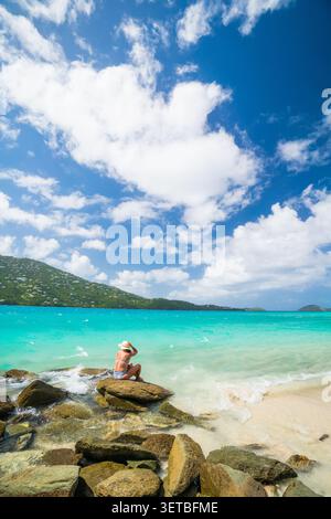 Una donna con un cappello da sole si rilassa su una spiaggia tropicale Foto Stock