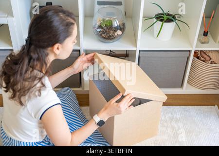 Giovane donna che apre il vano portaoggetti e cerca oggetti all'interno della casa. Organizzazione domestica e concetto di routine in declino Foto Stock
