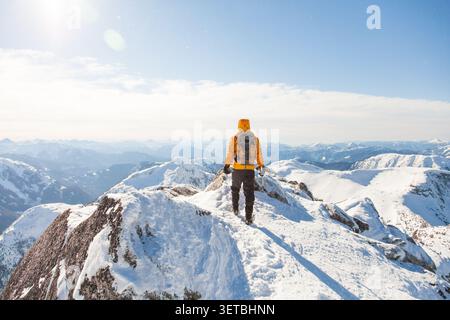 Alpinista in giacca gialla su una cima innevata Foto Stock